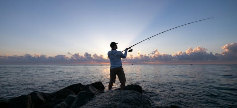 man in white t-shirt and brown shorts fishing on sea during daytime